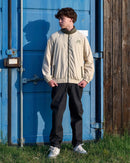 Person wearing a beige jacket with a logo standing in front of a blue container.