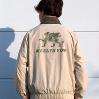 Person wearing a beige jacket with 'WEALTH VOW' logo on the back against a white wall.