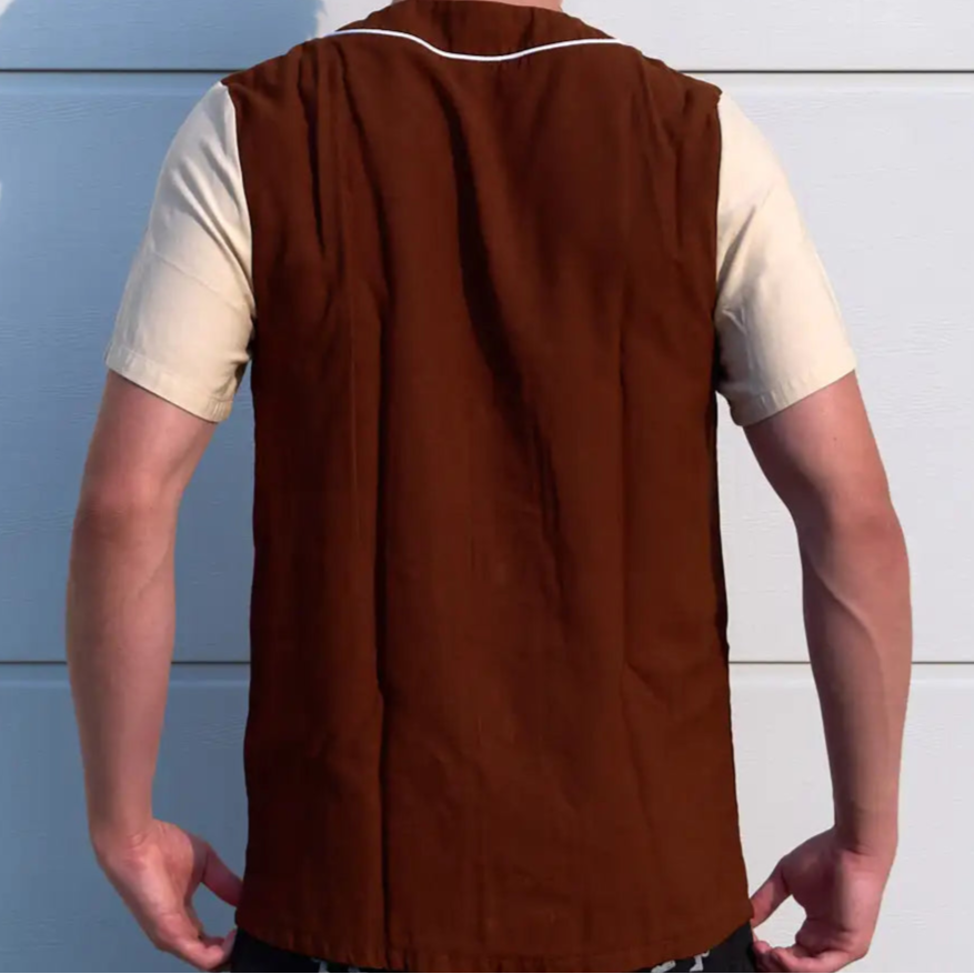 Person wearing a brown vest over a white shirt against a light blue wall